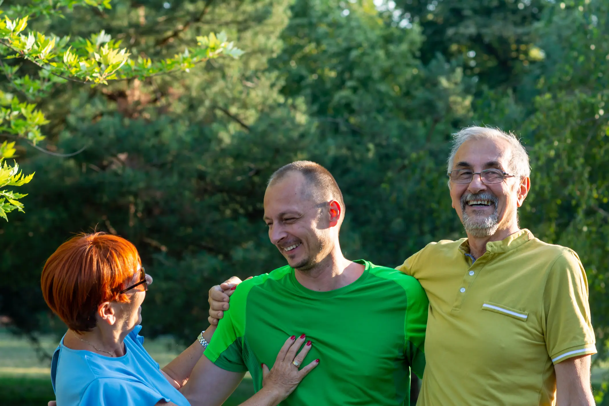 Three people laughing outdoors in sunlight.