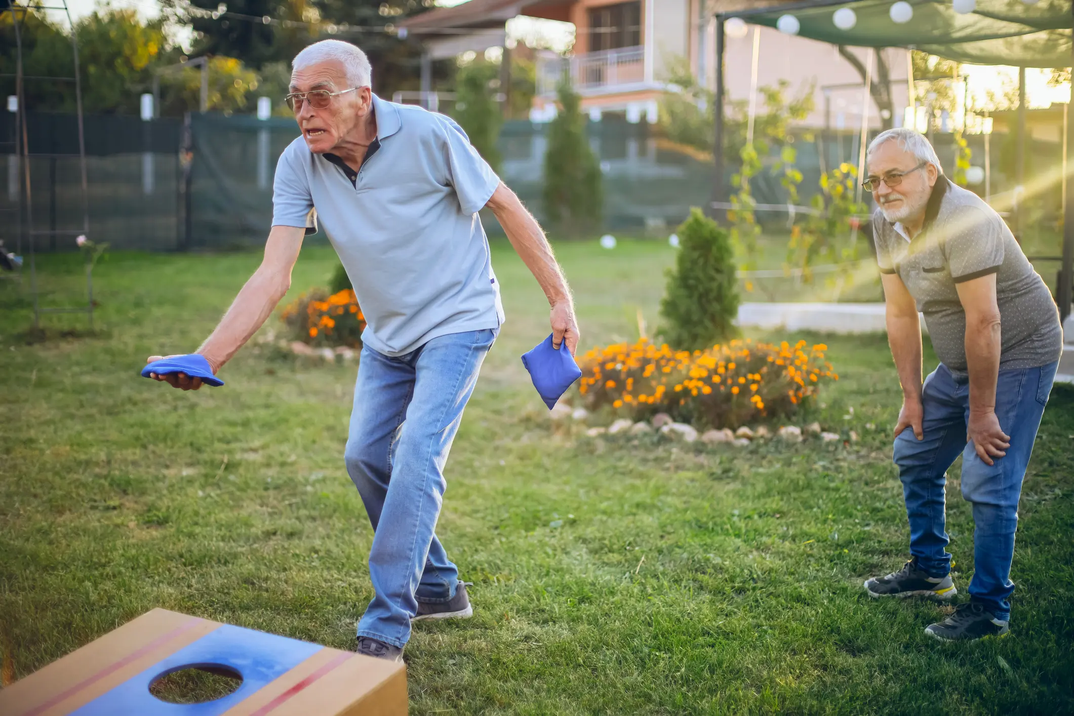 An elderly man playing cornhole outdoors on a sunny day.