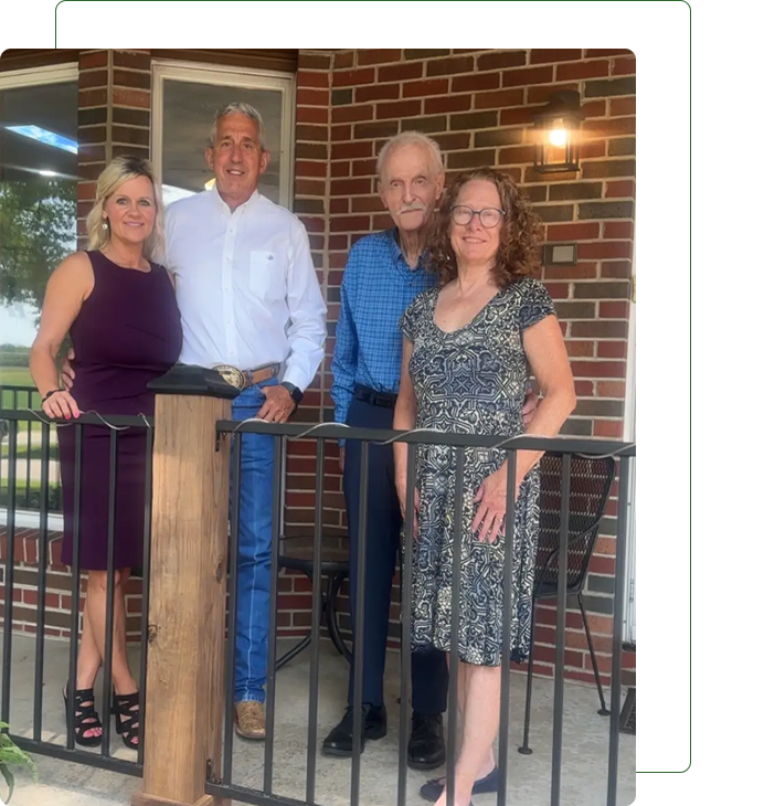 Four adults posing together indoors in front of a brick wall.