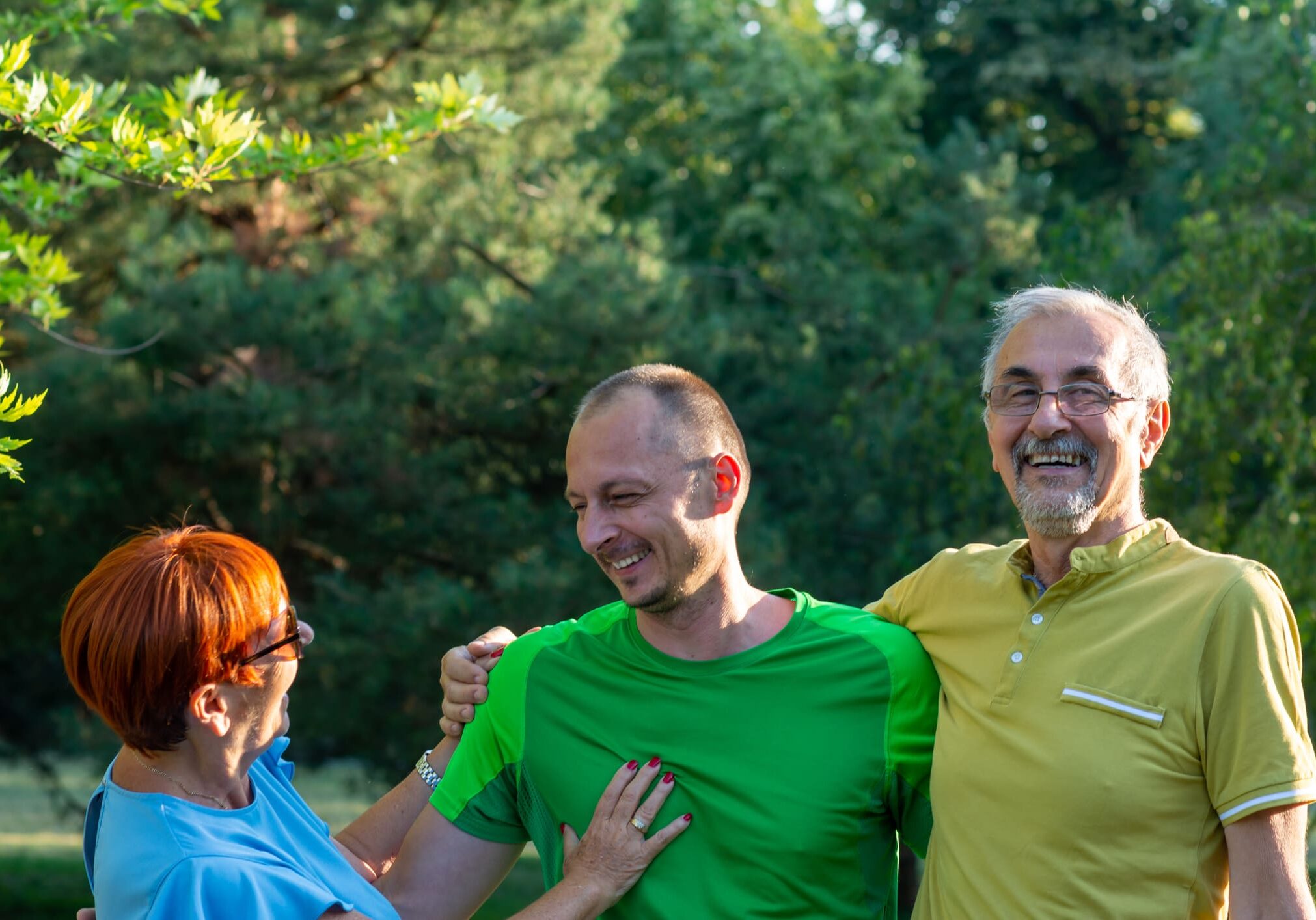 Three people laughing outdoors in sunlight.